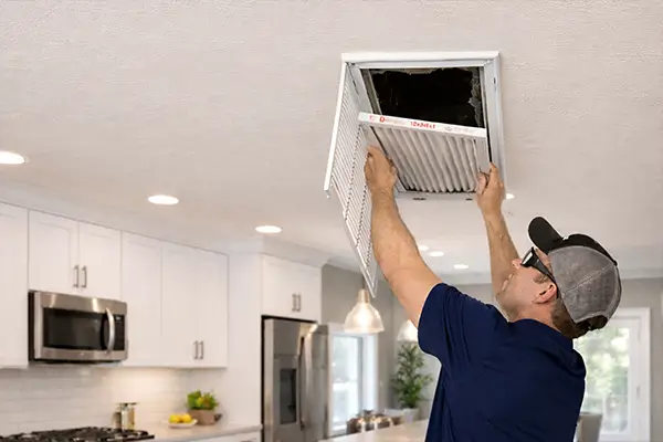 HVAC technician replacing ceiling air filter in modern kitchen